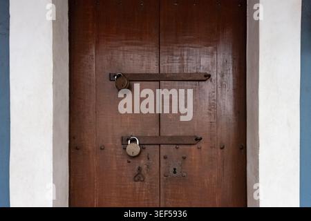 Grande porte en bois marron verrouillée avec un cadenas. Gros plan photo de la vieille porte en bois avec une double serrure rouillée. Personne, photo de rue Banque D'Images