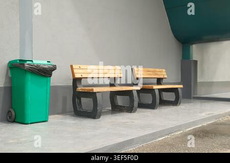 bancs en bois vides avec supports en béton et poubelle en plastique vert, mobilier urbain sur mur gris, vue latérale sur plateforme Banque D'Images
