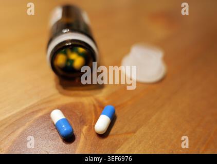 Pilules et capsules colorées renversant d'une bouteille pharmaceutique en verre ambré avec son couvercle ouvert sur une surface en bois, représentant un médicament, traitement Banque D'Images