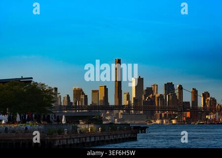 Les immenses gratte-ciel de Brooklyn s'élèvent bien en évidence derrière la structure en acier du pont de Williamsburg alors que la lumière dorée chaude frappe l'horizon urbain Banque D'Images