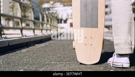 Derrière, jambes et skateboard avec personne en ville pour les déplacements écologiques ou les voyages sur le pont. Route asphaltée, baskets et transport avec homme Banque D'Images