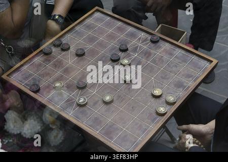 Jeu d'échecs chinois traditionnel xiangqi en cours sur planche de bois avec des pièces gravées, joueurs autour de la table, Vietnam Banque D'Images
