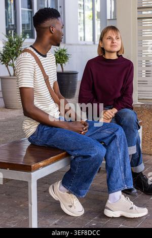 Amis hommes et femmes assis sur un banc en bois dans une cour couverte près des jardinières et des fenêtres Banque D'Images