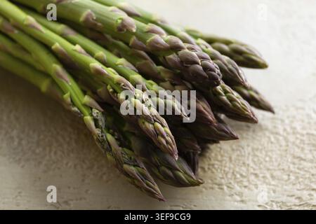 Un tas d'asperges vertes fraîches se trouve sur le comptoir de la cuisine. Les asperges ont des pointes serrées et fermes. Cette scène montre des aliments crus avant la préparation Banque D'Images
