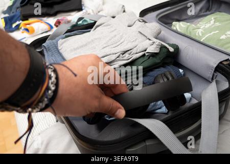 Personne emballant des écouteurs noirs dans une valise ouverte pleine de vêtements pour un voyage à venir Banque D'Images