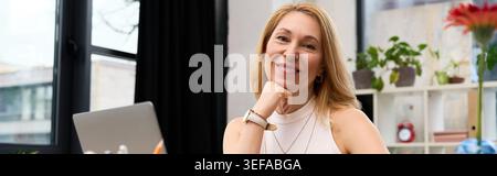 Une belle femme adulte est assise gracieusement à son bureau, rayonnant positivité et élégance. Banque D'Images