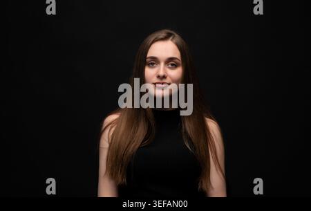 Portrait de jeune femme avec de longs cheveux bruns coulants semblant confiant et calme sur fond noir Banque D'Images
