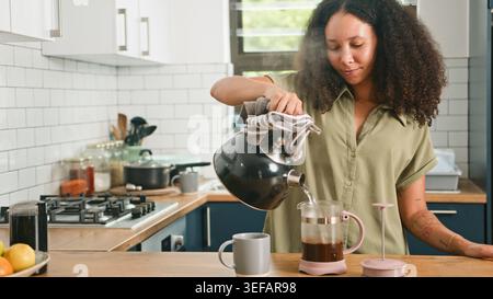 Femme versant de l'eau chaude de la bouilloire dans la presse française dans la routine du matin de la cuisine moderne Banque D'Images