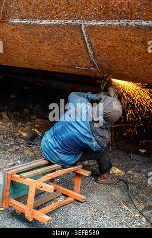 Des hommes réparent un bateau sur le chantier naval de Dhaka, au Bangladesh, pendant la journée, tandis que des étincelles s'échappent des travaux Banque D'Images