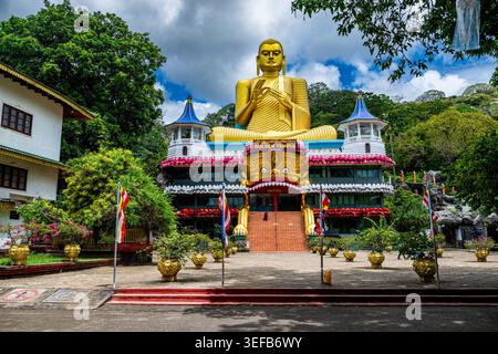 Statue de Bouddha doré au temple de la grotte de Dambulla au Sri Lanka entourée de verdure et de décorations colorées Banque D'Images