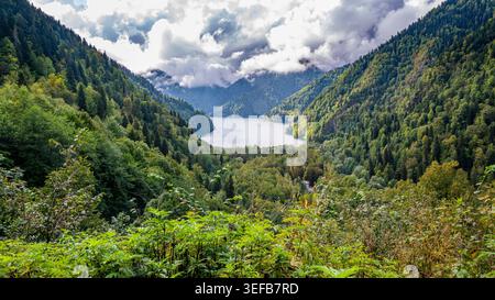 Vue depuis la vue sur le lac Ritsa montrant des montagnes et des forêts luxuriantes dans un paysage naturel avec des nuages au-dessus Banque D'Images