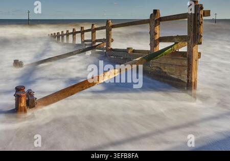 Les vagues s'écrasent autour d'un groyne sur la plage de Teignmouth, révélant la structure le long de la côte de la Manche dans le Devon Banque D'Images