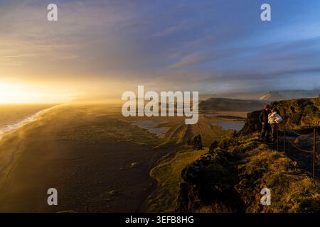Deux personnes apprécient la vue du coucher de soleil depuis les falaises de Dyrhlaey sur l'océan Atlantique en Islande Banque D'Images