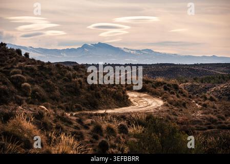 Chemin de terre sinueux à travers des collines arides menant à des montagnes en arrière-plan à Grenade, Andalousie, Espagne Banque D'Images