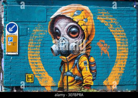 Peinture urbaine d'art de rue d'un personnage extraterrestre portant un costume jaune Hazmat et un masque respiratoire sur un fond de mur bleu à Brighton Banque D'Images