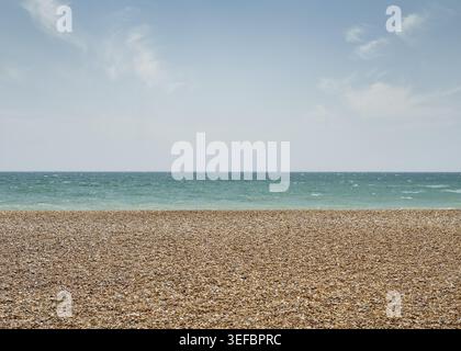 Large vue panoramique sur une plage de sable vide rencontrant une mer bleue calme sous un ciel pâle sur la côte à Brighton. Banque D'Images