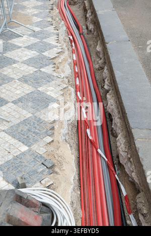 Divers fils électriques sont enfouis sous un passage de rue. Les pavés sont retirés pour permettre l'installation de câbles souterrains Banque D'Images