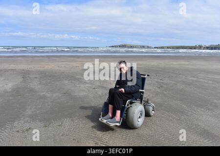 Homme assis dans un fauteuil roulant de plage, Poppit Sands Beach, Pembrokeshire, pays de Galles Banque D'Images