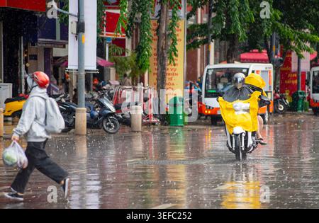 Les gens qui montent des motos portant des imperméables jaunes dans une rue pluvieuse à Ho Chi Minh-ville, Vietnam, avec des reflets sur l'asphalte humide Banque D'Images