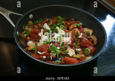 Légumes sautés tels que tomates, champignons, aubergines, poireaux et feta dans une poêle noire, repas végétarien sain, foyer sélectionné, étroit Banque D'Images
