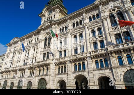 Façade néoclassique ornée du bâtiment de l'Hôtel de ville sur la Piazza Unità d'Italia avec tour de l'horloge et drapeaux nationaux sous un ciel bleu à Trieste, en Italie Banque D'Images