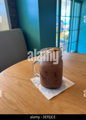 Une grande tasse en verre remplie de milkshake au chocolat ou de café glacé sur une table en bois. Banque D'Images