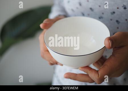 Tenant un bol blanc avec un design simple dans les mains Banque D'Images
