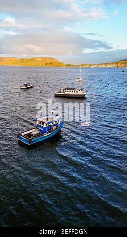Les bateaux colorés reposent paisiblement sur les eaux de la baie d'Oban tandis que la douce lumière du soir peint la côte écossaise dans des tons chauds et dorés Banque D'Images
