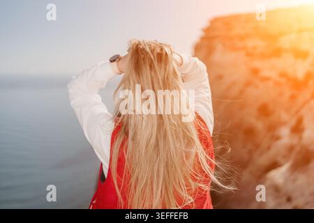 Femme coucher de soleil falaise debout sur le bord surplombant la mer tenant de longs cheveux blonds exprimant la liberté pendant l'heure dorée Banque D'Images