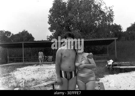 Sloviansk, 1983. Plage du camp pionnier de Vishnegorsk. Un portrait d'archives classique en noir et blanc montrant frère et sœur, Dmitri Mikhailovitch Kravelis et Inessa Mikhailovna Kravelis, debout ensemble sur le sable. Dmitry porte un maillot de bain rayé et Inessa porte un maillot de bain rayé élégant. Ils sourient chaleureusement sous le soleil brillant près de la canopée d'ombre du camp. Cette photographie authentique préserve des souvenirs agréables de jeunesse, des liens familiaux et des vacances d'été paisibles à l'ère d'un Donbass paisible. Banque D'Images