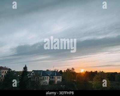 Valka, Lettonie - 8 mai 2026 : paysage de campagne atmosphérique avec une vieille maison rurale sous des nuages spectaculaires au coucher du soleil. Décor de soirée serein Banque D'Images