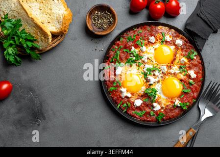 Shakshuka - oeufs frits dans une sauce tomate épicée, nappés de fromage feta et de persil dans une poêle en fonte. Shakshuka - petit-déjeuner méditerranéen Helthy sur conc Banque D'Images