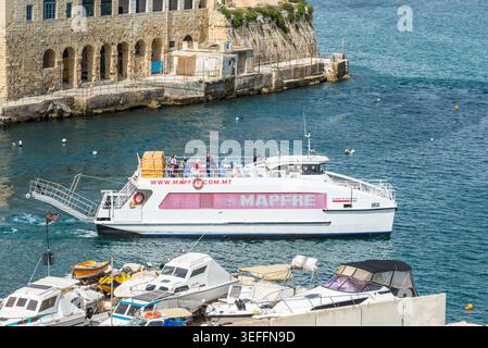 La Valette, Malte – 16 mai 2025 : ferry Sliema-Valletta naviguant à travers le port historique, avec des passagers sur le pont et architecture en pierre au bord de l'eau Banque D'Images