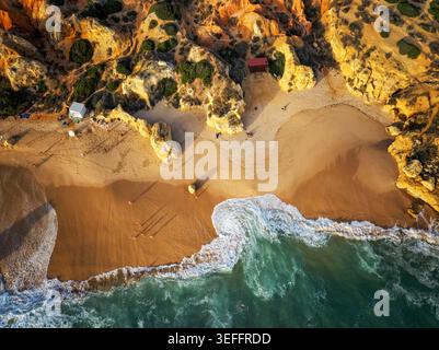 Vue aérienne de haut en bas des vagues lavant sur la plage de Praia de Sao Rafael à côté des falaises dorées de l'Algarve. Banque D'Images