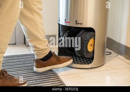 Une vue rapprochée montre une personne plaçant une chaussure en cuir dans un dispositif de polissage électrique avec des brosses motorisées pour nettoyer les chaussures efficacement, à la hauteur Banque D'Images