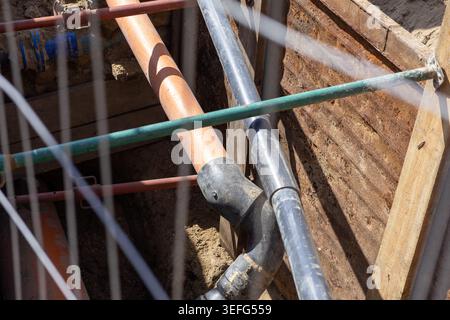 Tranchée profonde révélant des canalisations d'égout souterraines et un conduit orange soutenus par des entretoises métalliques temporaires pour la sécurité du site industriel pendant la période municipale Banque D'Images