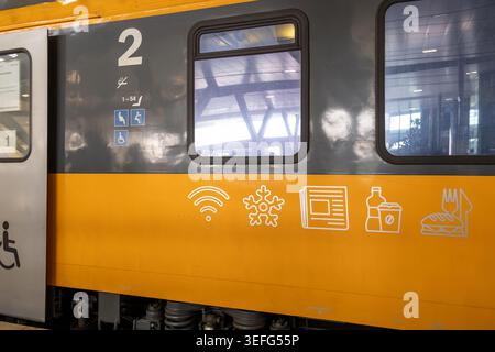Vue latérale d'un wagon jaune affichant des symboles pour l'Internet sans fil, le contrôle de la climatisation et la restauration, mettant en évidence les équipements de voyage modernes A. Banque D'Images