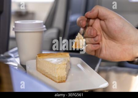 Un passager tient une fourchette avec un morceau de cheesecake à côté d'une tasse à café jetable sur un plateau d'avion, mettant en évidence le repas de voyage, les loisirs, et le c. Banque D'Images