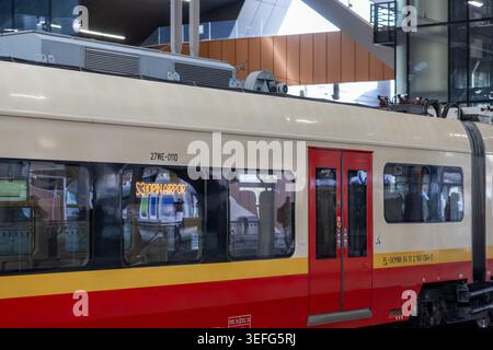 Varsovie, Pologne - 13 avril 2026 : vue latérale d'une voiture de train électrique garée sur un quai de gare avec une signalisation lumineuse indiquant la route de l'aéroport vers fac Banque D'Images