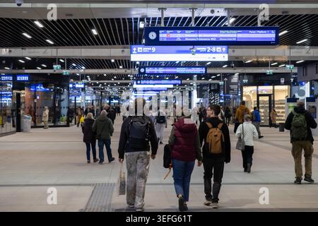 Varsovie, Pologne - 13 avril 2026 : les voyageurs avec des sacs à dos marchent à l'intérieur d'un hall de gare moderne avec des tableaux d'horaires électroniques pour représenter quotidiennement t Banque D'Images