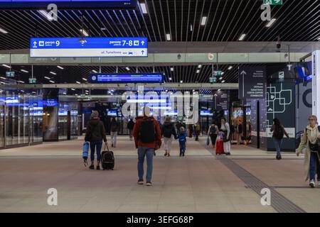 Varsovie, Pologne - 13 avril 2026 : les voyageurs avec des valises traversent une gare ferroviaire moderne et animée de Varsovie, avec un panneau de navigation clair Banque D'Images