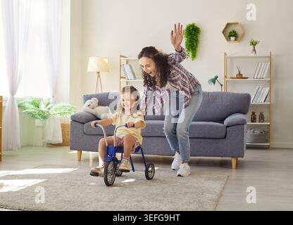 Maman prend en charge la fille en tricycle à la maison, apprentissage ludique dans le salon Banque D'Images