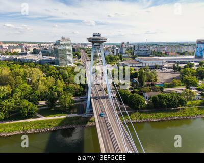 Vue aérienne de la plupart des ponts SNP avec son emblématique pont d'observation des OVNIS enjambant le Danube entouré d'arbres verdoyants et de l'horizon de la ville brat Banque D'Images