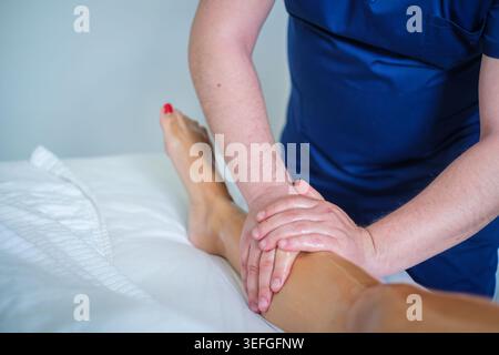Une femme reçoit un massage relaxant des mollets dans un salon de spa par un thérapeute professionnel utilisant de l'huile pour le drainage lymphatique. Banque D'Images