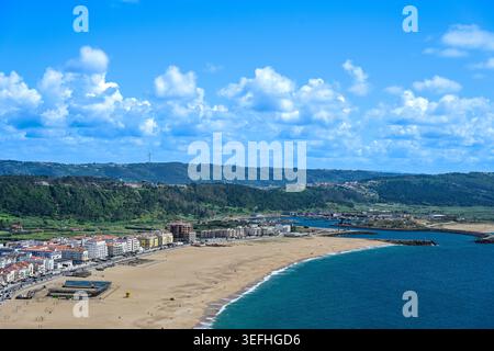 Paysage côtier panoramique de Nazaré, Portugal, avec plages de sable, eaux turquoises de l'Atlantique, collines ondulantes, et des cieux spectaculaires remplis de nuages. Banque D'Images