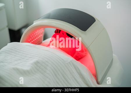 Le client subit un nettoyage du visage avec la luminothérapie LED pour cibler l'acné tout en étant protégé par des lunettes de protection et un chapeau de cheveux pour le confort. Banque D'Images