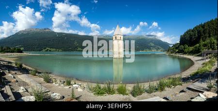 Vue sur le clocher immergé historique de Reschensee debout dans l'eau turquoise entouré de montagnes verdoyantes Graun im Vinschgau, Trentin Banque D'Images