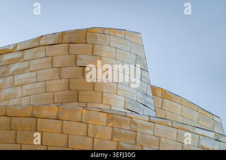 Vue des panneaux de titane courbés du Musée Guggenheim Bilbao reflétant la lumière dorée contre un ciel dégagé à Bilbao, Euskadi, Espagne. Banque D'Images