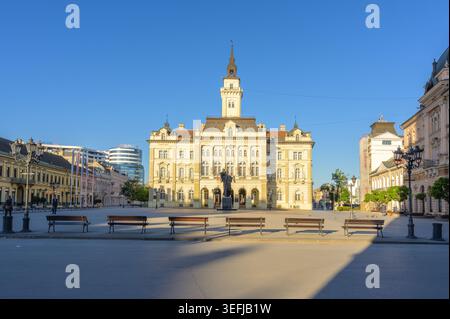 L'hôtel de ville de Novi Sad se trouve bien en vue sur la place de la liberté, présentant l'architecture européenne historique sous un ciel bleu clair. Cette capture de paysage urbain Banque D'Images