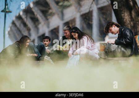 Des amis d'école étudient ensemble à l'extérieur sur le banc du campus partageant des livres et des conversations Banque D'Images